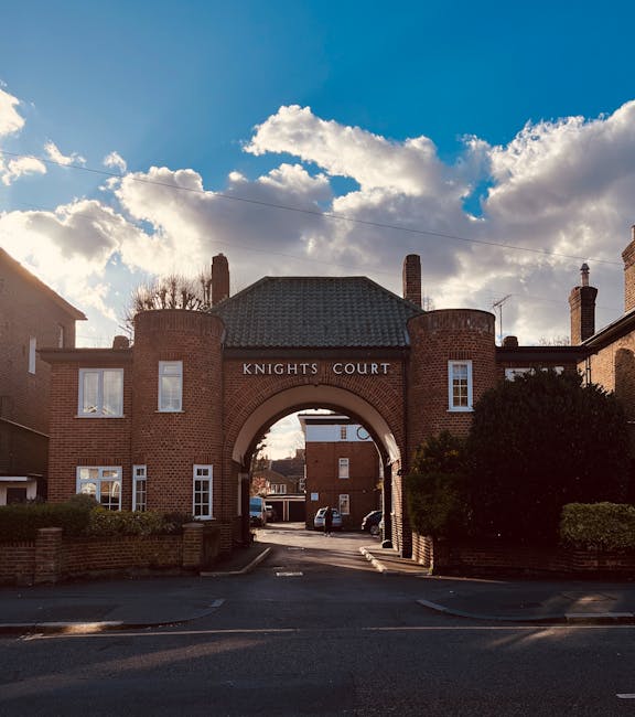 A wide shot of the entrance to Knights Court, a residential development featuring a large, brick archway with a curved top, flanked by two rounded brick towers. The archway has the name 'KNIGHTS COURT